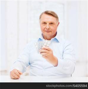 healthcare, madicine, pharmacy and elderly concept - old man with pack of pills
