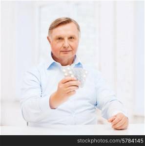 healthcare, madicine, pharmacy and elderly concept - old man with pack of pills