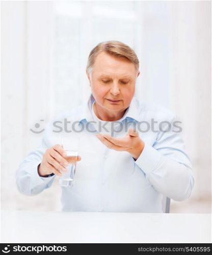 healthcare, madicine, pharmacy and elderly concept - old man with pills and glass of water