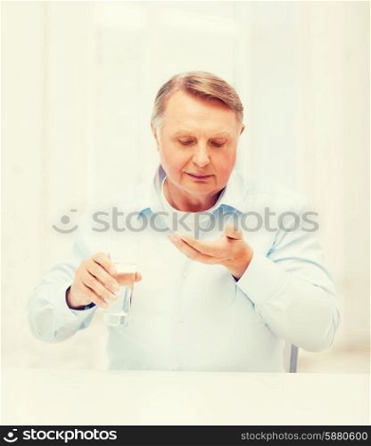 healthcare, madicine, pharmacy and elderly concept - old man with pills and glass of water