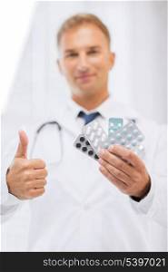 healthcare, medical and pharmacy concept - male doctor with packs of pills showing thumbs up
