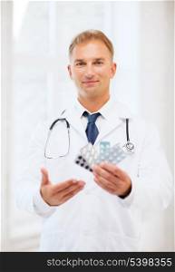 healthcare, medical and pharmacy concept - young male doctor with packs of pills