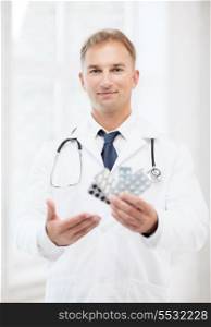 healthcare, medical and pharmacy concept - young male doctor with packs of pills