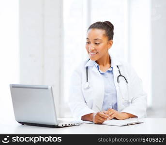 healthcare, medical and technology concept - african female doctor with laptop pc writing prescription