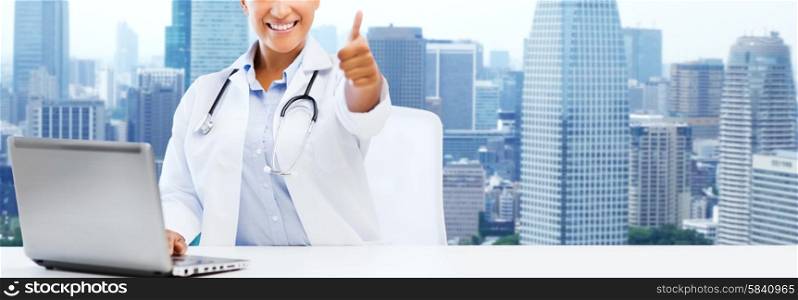 healthcare, medical and technology concept - happy african american female doctor with laptop pc computer showing thumbs up over city background
