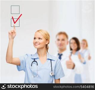 healthcare, medical and technology - young doctor or nurse with marker drawning red checkmark into checkbox with team on the back