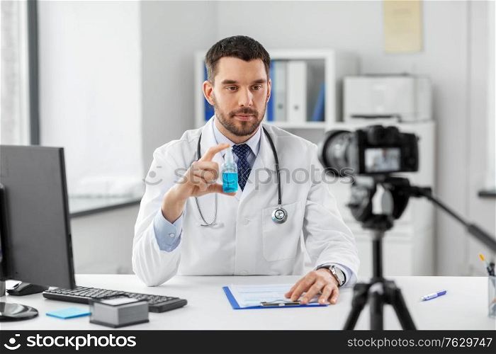 healthcare, medicine and blogging concept - male doctor with camera and hand sanitizer recording video blog at hospital. doctor with hand sanitizer recording video blog