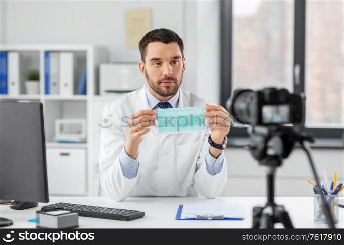 healthcare, medicine and blogging concept - male doctor with camera protective face mask drug and recording video blog at hospital. doctor with mask recording video blog at hospital