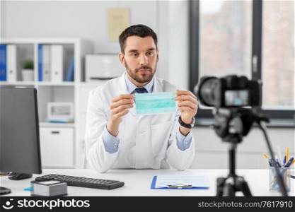 healthcare, medicine and blogging concept - male doctor with camera protective face mask drug and recording video blog at hospital. doctor with mask recording video blog at hospital