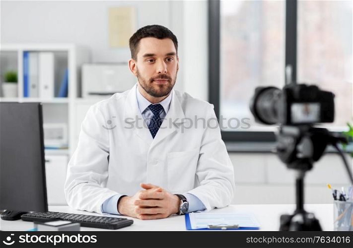 healthcare, medicine and blogging concept - male doctor with camera recording video blog at hospital. male doctor recording video blog at hospital