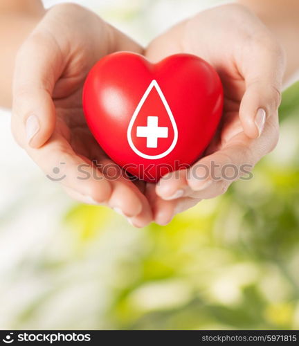 healthcare, medicine and blood donation concept - female hands holding red heart with donor sign over green natural background