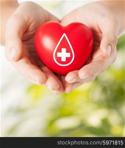 healthcare, medicine and blood donation concept - female hands holding red heart with donor sign over green natural background