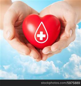 healthcare, medicine and blood donation concept - female hands holding red heart with donor sign over blue sky and clouds background