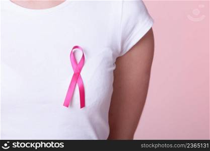 Healthcare, medicine and breast cancer awareness concept - Closeup of pink badge ribbon on woman chest to support breast cancer cause. Pink ribbon on woman chest to support breast cancer cause