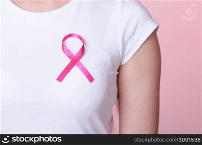 Healthcare, medicine and breast cancer awareness concept - Closeup of pink badge ribbon on woman chest to support breast cancer cause. Pink ribbon on woman chest to support breast cancer cause