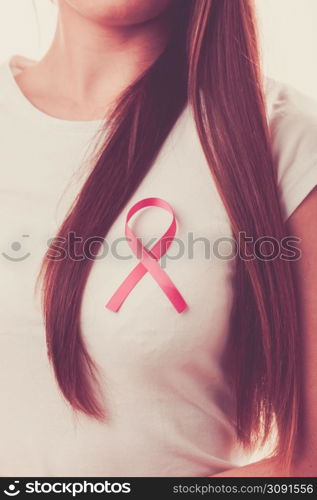 Healthcare, medicine and breast cancer awareness concept - Closeup of pink badge ribbon on woman chest to support breast cancer cause. Pink ribbon on woman chest to support breast cancer cause