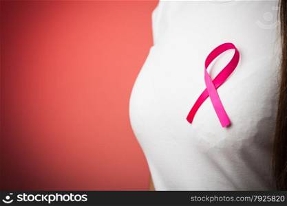 Healthcare, medicine and breast cancer awareness concept - Closeup of pink badge ribbon on woman chest to support breast cancer cause on red