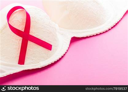 Healthcare, medicine and breast cancer awareness concept. Closeup pink ribbon on female bra over pink background.