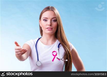 Healthcare, medicine and breast cancer awareness concept. Doctor with pink ribbon aids symbol, inviting making welcome hand gesture on blue. Woman pink ribbon on chest making welcome gesture