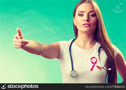 Healthcare, medicine and breast cancer awareness concept. Doctor with pink ribbon aids symbol, inviting making welcome hand gesture on green. Woman pink ribbon on chest making welcome gesture