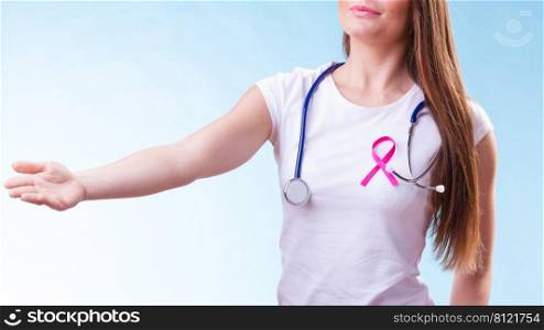 Healthcare, medicine and breast cancer awareness concept. Doctor with pink ribbon aids symbol, inviting making welcome hand gesture on blue. Woman pink ribbon on chest making welcome gesture