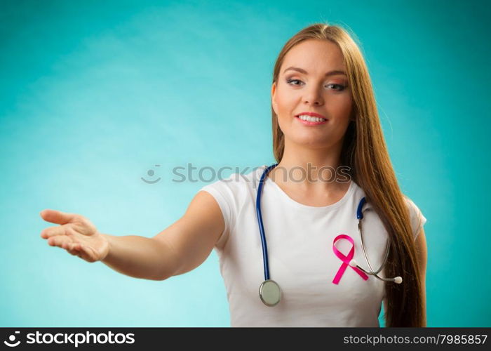 Healthcare, medicine and breast cancer awareness concept. Doctor with pink ribbon formed Aids symbol, inviting making welcome hand gestureon blue