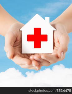 healthcare, medicine and charity concept - hands holding white paper house with red cross sign