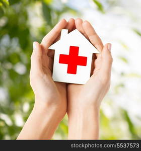 healthcare, medicine and charity concept - hands holding white paper house with red cross sign