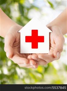 healthcare, medicine and charity concept - hands holding white paper house with red cross sign