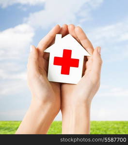 healthcare, medicine and charity concept - hands holding white paper house with red cross sign