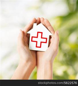 healthcare, medicine and charity concept - hands holding white paper house with red cross sign