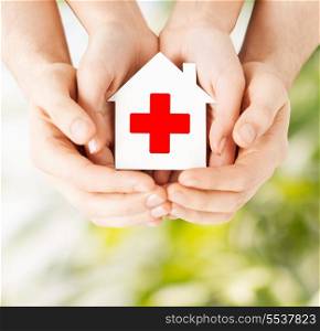 healthcare, medicine and charity concept - male and female hands holding white paper house with red cross sign