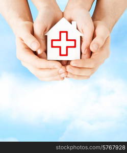healthcare, medicine and charity concept - male and female hands holding white paper house with red cross sign