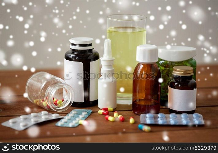 healthcare, medicine and drugs concept - pills, nasal spray, antipyretic syrup and glass on wooden table over snow. medicine and drugs on wooden table