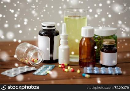 healthcare, medicine and drugs concept - pills, nasal spray, antipyretic syrup and glass on wooden table over snow. medicine and drugs on wooden table