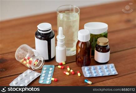 healthcare, medicine and drugs concept - pills, nasal spray, antipyretic syrup and glass on wooden table