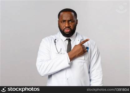 Healthcare, medicine and epidemic concept. Serious-looking angry and frustrated african-american doctor scolding patient not taking care health, pointing finger right and stare with judgement.. Healthcare, medicine and epidemic concept. Serious-looking angry and frustrated african-american doctor scolding patient not taking care health, pointing finger right and stare with judgement