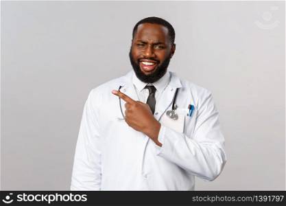 Healthcare, medicine and epidemic concept. Skeptical and judgemental african-american doctor judging people treating virus symptoms with homeopathy, grimace and pointing finger left.. Healthcare, medicine and epidemic concept. Skeptical and judgemental african-american doctor judging people treating virus symptoms with homeopathy, grimace and pointing finger left