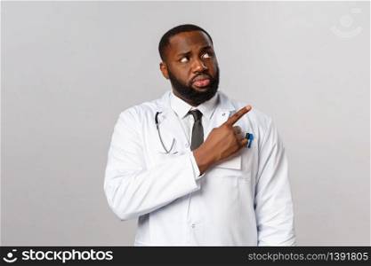 Healthcare, medicine and epidemic concept. Skeptical, hesitant african-american doctor seeing someone advice use homeopathy look doubts at promo, pointing upper right corner.. Healthcare, medicine and epidemic concept. Skeptical, hesitant african-american doctor seeing someone advice use homeopathy look doubts at promo, pointing upper right corner