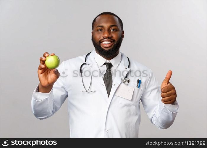 Healthcare, medicine and healthy lifestyle concept. Confident handsome african-american doctor recommend eat fruits, hold green apple, smiling pleased and thumb-up, patient need vitamins.. Healthcare, medicine and healthy lifestyle concept. Confident handsome african-american doctor recommend eat fruits, hold green apple, smiling pleased and thumb-up, patient need vitamins