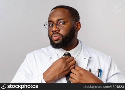 Healthcare, medicine and hospital treatment concept. Confident african-american doctor fixing tie, put-on white coat for work, having night shift at clinic to treat patients with covid-19 symptoms.. Healthcare, medicine and hospital treatment concept. Confident african-american doctor fixing tie, put-on white coat for work, having night shift at clinic to treat patients with covid-19 symptoms