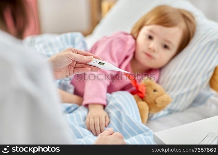 healthcare, medicine and people concept - close up of doctor with thermometer measuring temperature of little sick girl lying in bed at home. doctor measuring sick girl&rsquo;s temperature