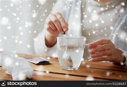 healthcare, medicine and people concept - close up of ill woman stirring medication in cup with spoon over snow. ill woman stirring medication in cup with spoon