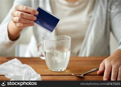 healthcare, medicine and people concept - close up of woman pouring medication into cup of water and paper tissue on wooden table