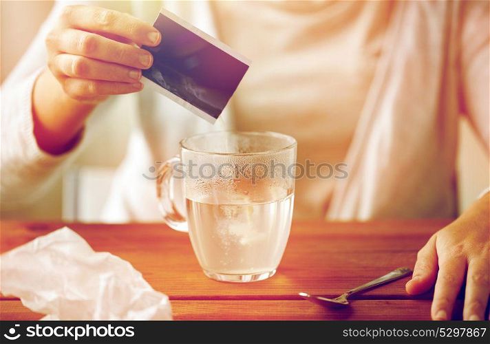 healthcare, medicine and people concept - close up of woman pouring medication into cup of water and paper tissue on wooden table. woman pouring medication into cup of water