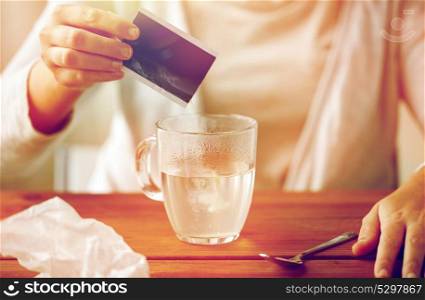 healthcare, medicine and people concept - close up of woman pouring medication into cup of water and paper tissue on wooden table. woman pouring medication into cup of water