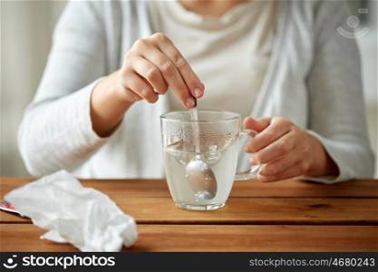 healthcare, medicine and people concept - close up of woman stirring medication in cup with spoon and paper tissue on wooden table