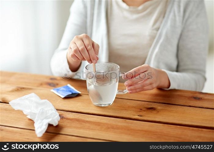 healthcare, medicine and people concept - close up of woman stirring medication in cup with spoon and paper tissue on wooden table