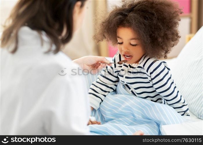 healthcare, medicine and people concept - doctor giving cough syrup to little sick african american girl in bed at home. doctor giving medicine to sick girl in bed at home