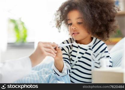 healthcare, medicine and people concept - doctor showing thermometer to happy smiling sick little african american girl in bed at home. doctor showing thermometer to smiling sick girl